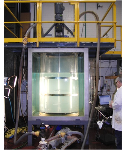 Solvent extraction equipment with chemist. Looks like a large glass cylindrical tank filled with clear fluid.