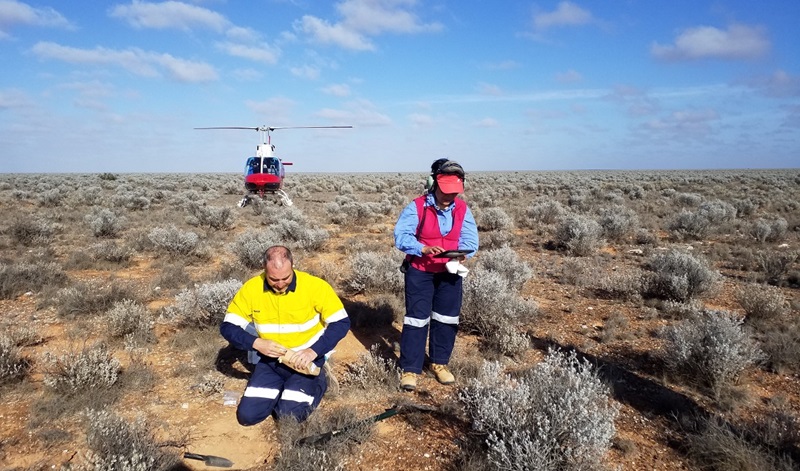 Male and female scientists taking soil sample in remote area using a helicoptor to move from place to place