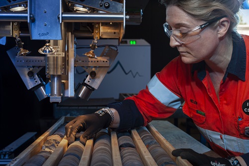 Female researcher touching cylindrical drill core segments processed through machine 