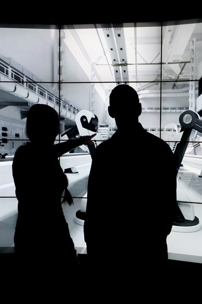 Sillouette of two people infront of screen showing robots in a factory