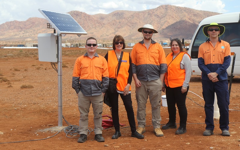 Group of five researcher in high vis clothing stadning against red dirt landscape