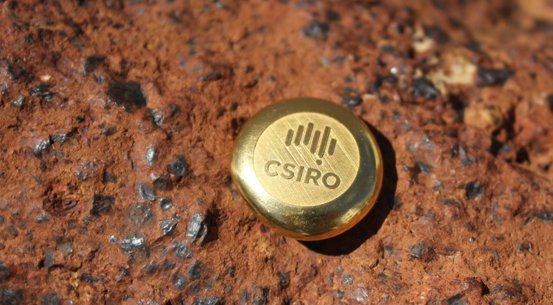 Gold ingot engraved with the CSIRO logo on rocky background
