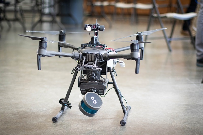 Four pronged flying drone fitted with a cylindrical unit housing scanning camera 