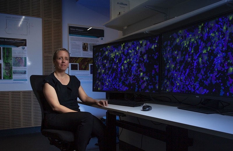 Dr Louise Fisher sitting in front of bright colourful images on computer screens