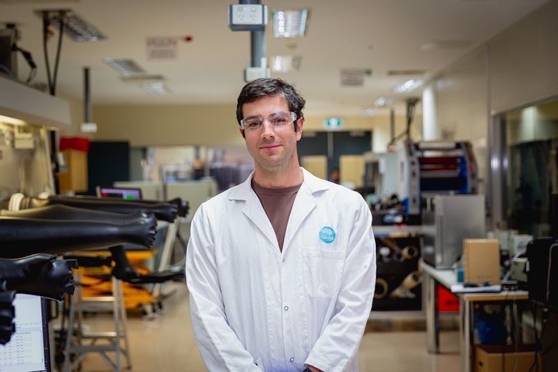Dr Anthony Chesman is Group Leader of the Renewable Energy Systems Group. He is in the centre of the frame in a lab coat standing in front of lab equipment.