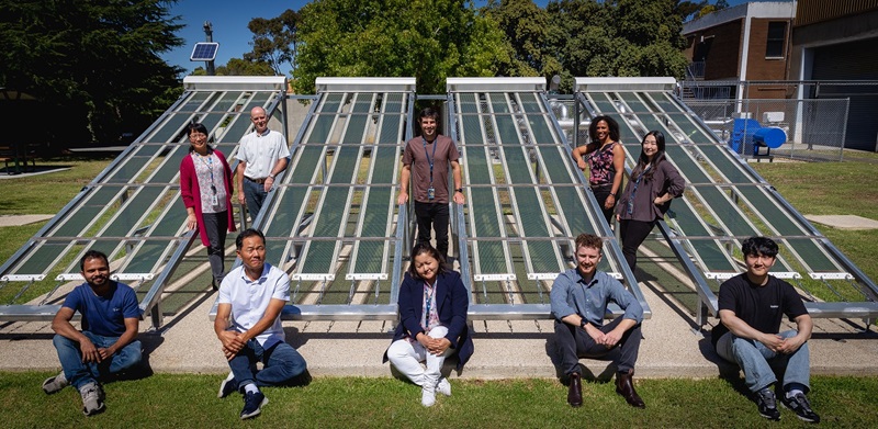CSIRO's printed flexible solar team members sitting between a large outdoor display of printed flexible solar