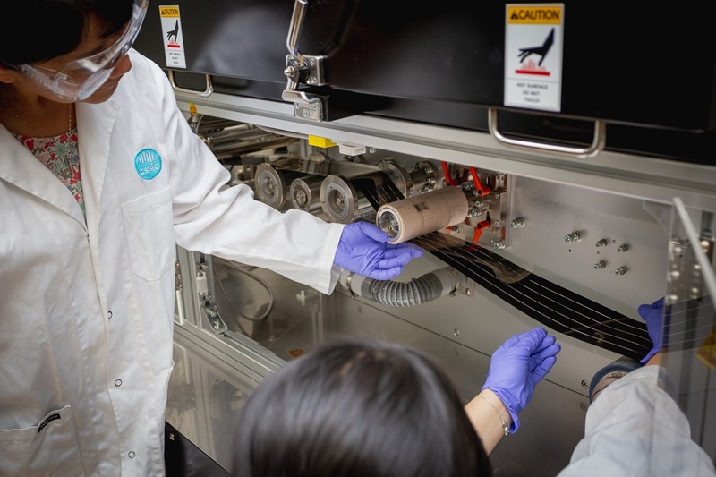 CSIRO Scientist Dr Mei Gao, wearing a lab coat and looking at roll-to-roll solar cell printer