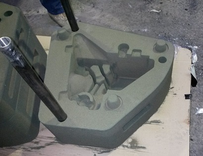 A large grey/green casting mould of a complicated shape - for a component of the Hawkei vehicle. It is sitting on a piece of cardboard on the floor of the CSIRO Lab.