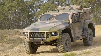 Camouflaged army vehicle (The Hawkei Protected Mobility Vehicle) driving on bush track, with bushland inbackground