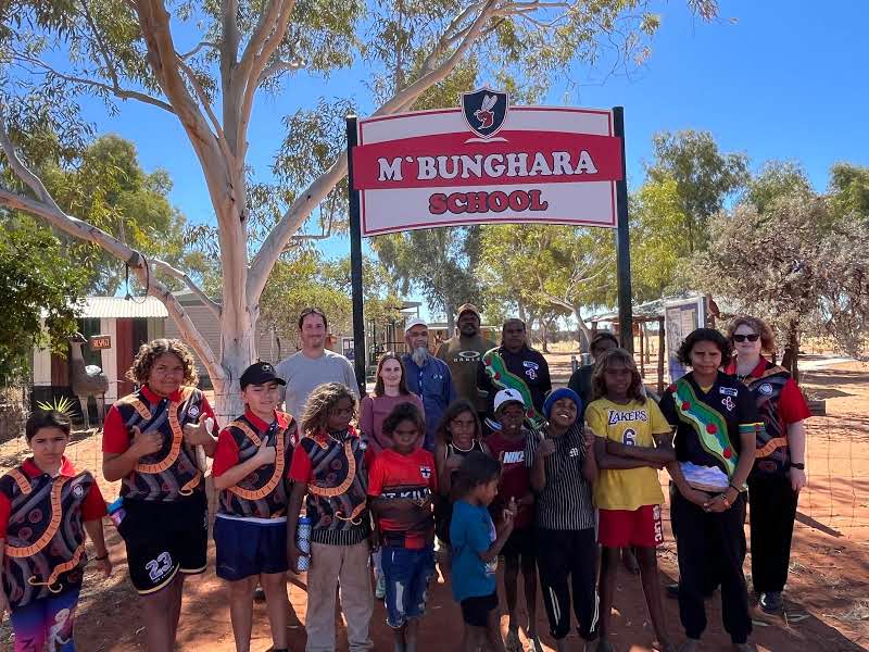 A group of students, teachers and CSIRO scientists in front of a sign at M'Bunghara school