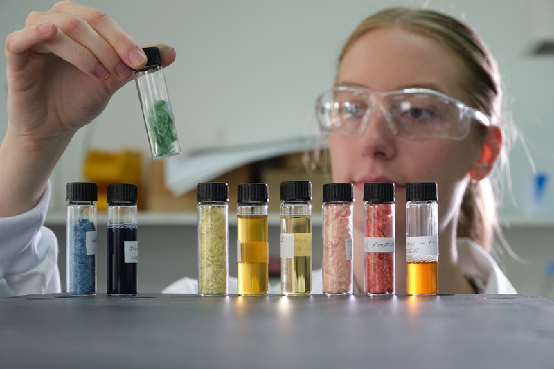 Image of CSIRO chemist Nicola spencer looking at small glass containers with different coloured silk dyed. 