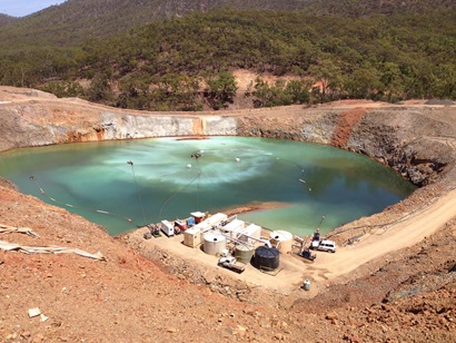 A pit filled with mining wastewater with several tanks on the bank and pipes leading into the water.