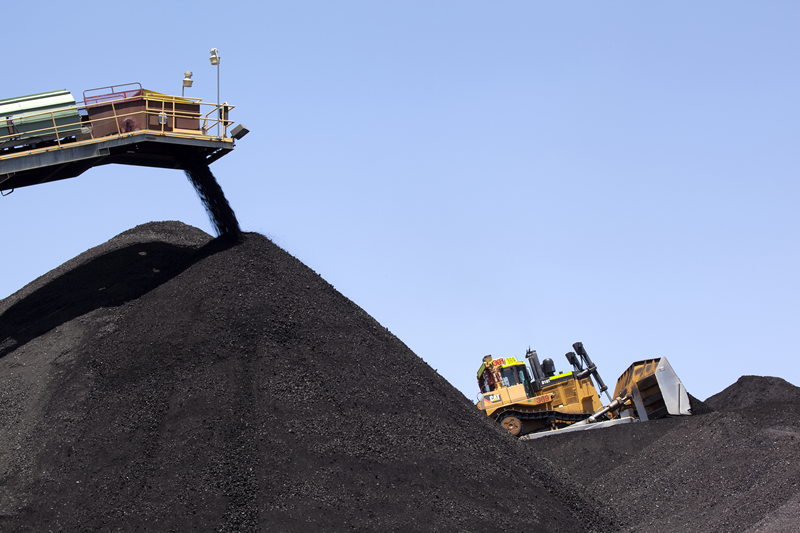 Coal loading adding to large pile of coal with yellow truck in background
