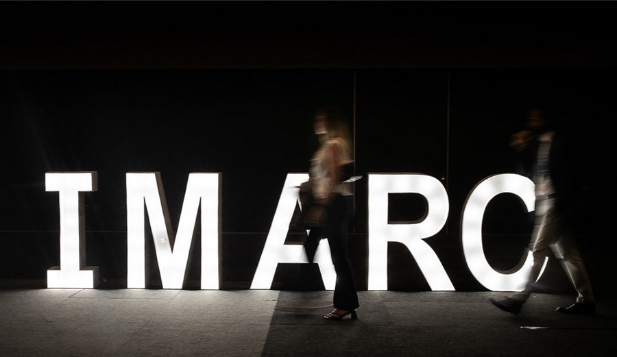 Illuminated IMARC sign with people walking past