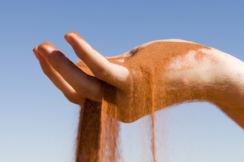 Red sand flowing through the fingers of an outstretched hand