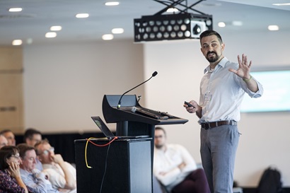 Man standing at lectern pointing at screen
