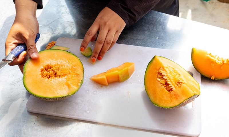 A medium close up of a person cutting up rock melon on a cutting board