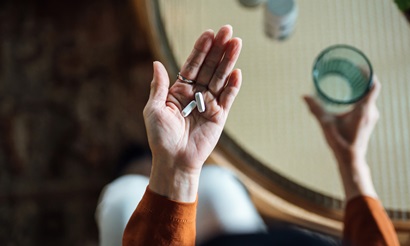 Overhead view of a person holding antimicrobial tablets in one hand, and a glass of water in the other