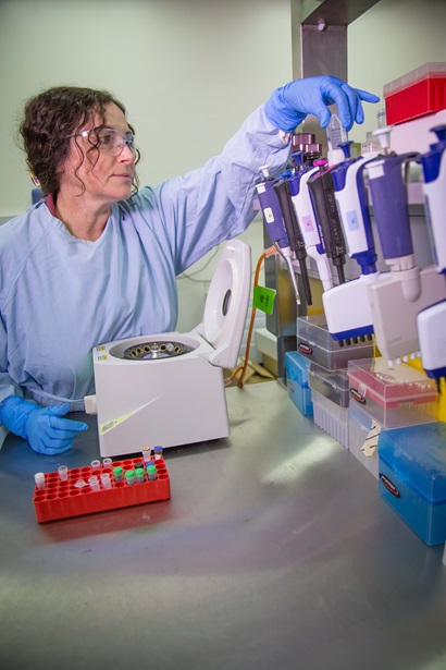 A female scientist in blue lab coat working at a lab bench.