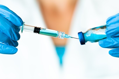 Scientist wearing blue rubber gloves extracting solution from a vial using a syringe.