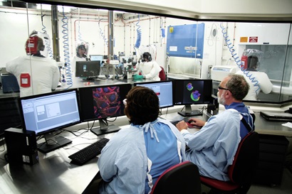Scientists working in the Control Room looking into the PC4 Zoonosis laboratory and Bioimaging Facility.