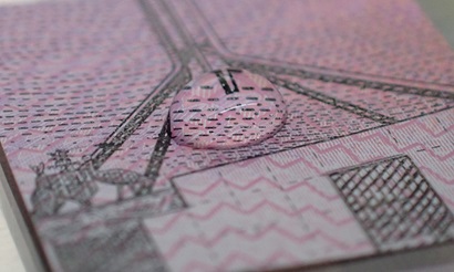 A droplet of liquid forming a circular mound in the middle of a small sqaure of cut Australian five dollar banknote.