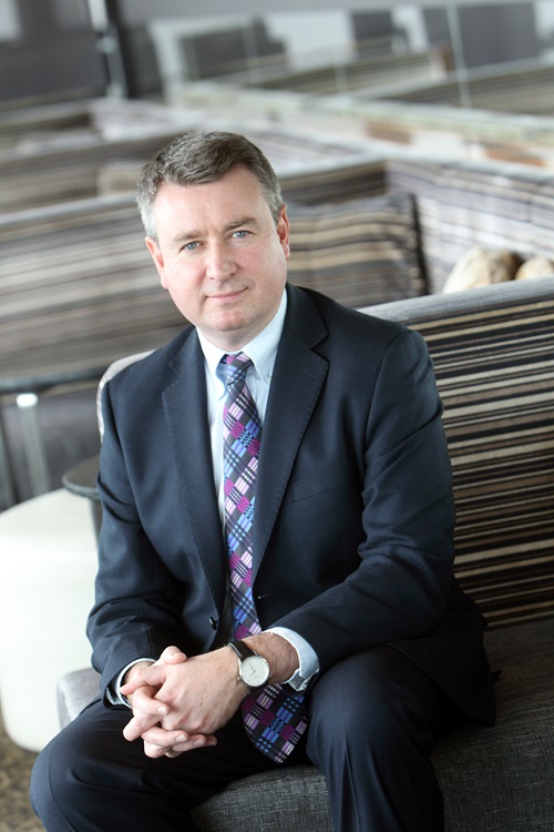 Dr Ian Oppermann wearing a suit and tie sits on bench.