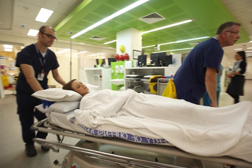 A young patient arriving in hospital emergency on a stretcher with two medical staff attending.