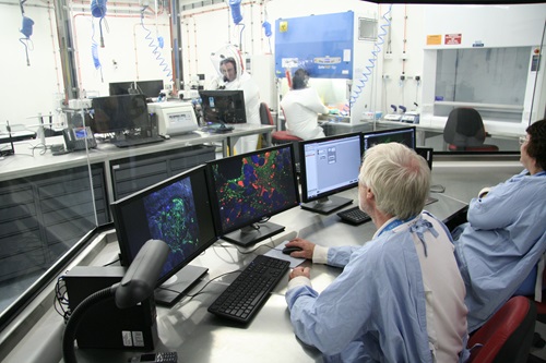 Scientists sitting behind a bank of computers observing other scientists within a secure laboratory environment