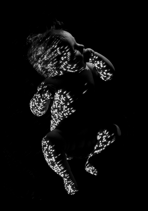 Black and white photo of a baby with white shapes reflected on skin.