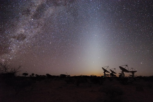 View of a starry night sky with radio telescopes in the background.