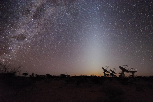 View of a starry night sky with radio telescopes in the background.