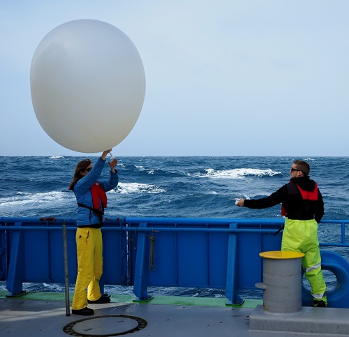 Two scientists deploy a weather balloon from the RV Investigator.