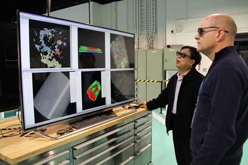 Two men standing in front of a large computer screen showing Lab 22 technology in use.