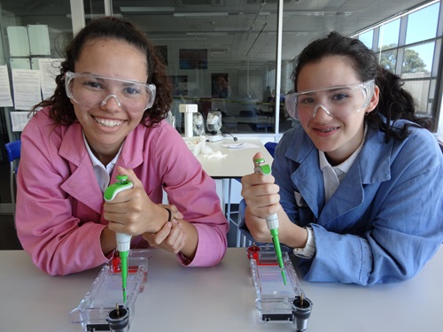 Two students holding pipettes at a lab bench.