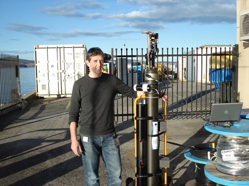 Nick Hardman-Mountford standing on a warf, resting arm on a BioArgo robotic float.
