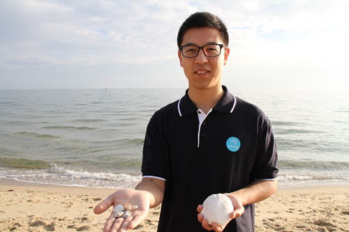 Dr Kang Liang holding an assortment of small seashells in one hand and a large seashell in the other.