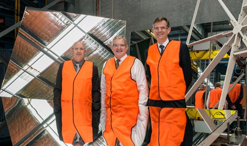 Three men in high visibility vests inspect a heliostat.