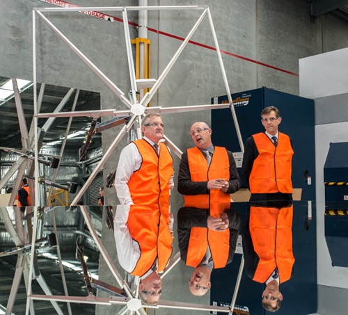 Three men in high visibility vests inspect a heliostat.