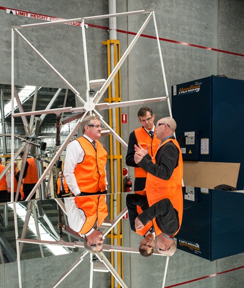 Three men in high visibility vests talk in front of a heliostat.