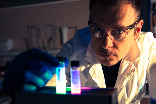 Paolo Falcaro in a lab coat and safety glasses holding a vial.
