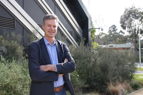 Dr Rob Grenfell standing with arms folded in front of building and garden.
