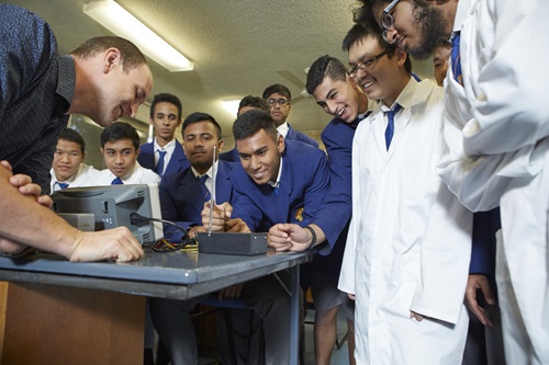 Teacher and students standing around a lab desk watching an experiment. 