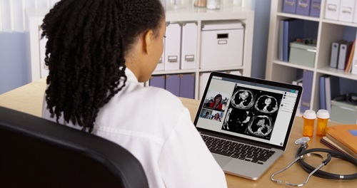 Doctor sitting in front of laptop showing Data61's Coviu audio-video platform.
