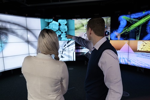 Two people looking at a wall of electronic screens.