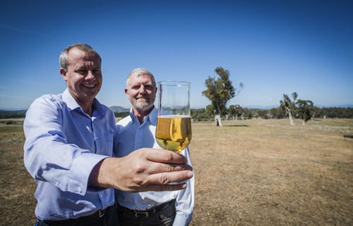 Dr Crispin Howitt and Dr Phil Larkin stand in a field, holding a glass of beer