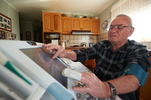 Man with sensor on a finger using the screen of the home monitoring telehealth device.