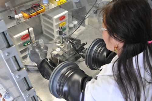 A female researcher works using a glovebox in a lab environment.