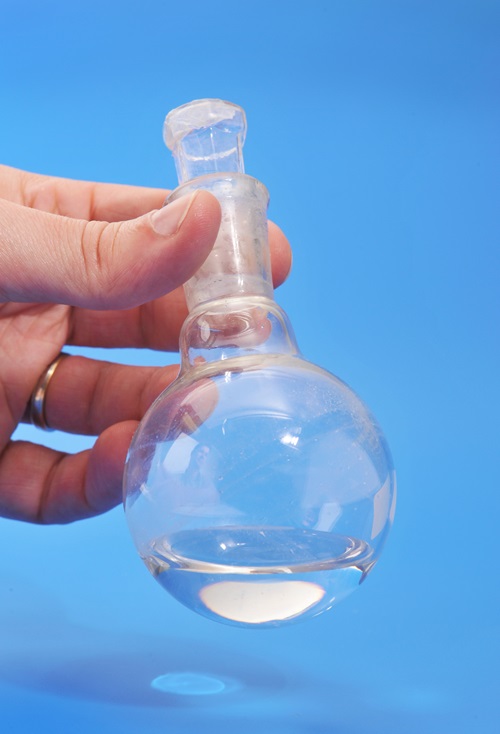 A hand holds a glass beaker with clear fluid in it.