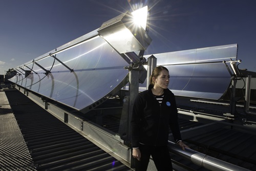 A woman stands in front of rooftop concentrating solar thermal collectors